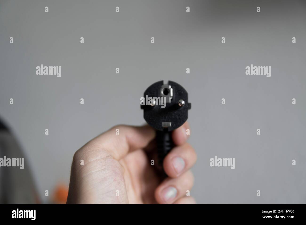 Hand holding black electric plug on a grey background. Stock Photo