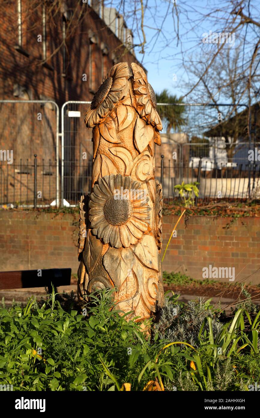 A large piece of wooden sculpture showing Sunflower heads and leaves built into a small round walled planter outside the local shops. Stock Photo