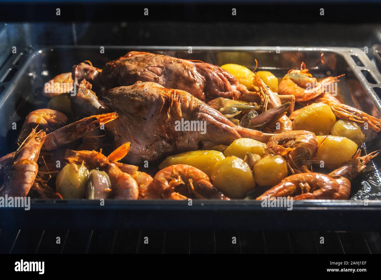 Kid meat baked in the oven with some potatoes, prawns, shrimps and vegetables. Family event and gathering dinner with empty copy space. Stock Photo