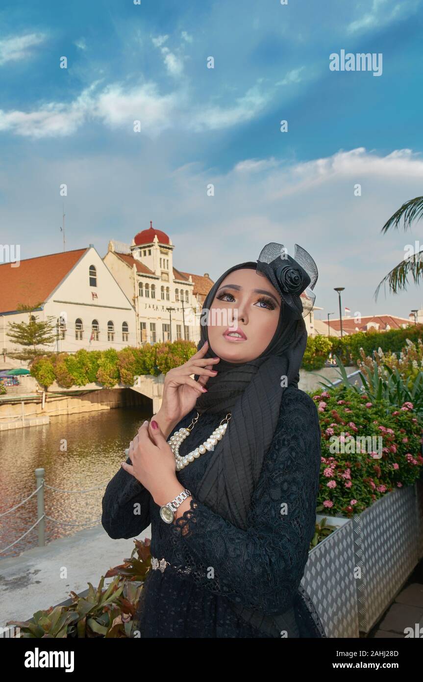 young lady wearing black hijab on a sunny afternoon looking at the sky wearing a pearl necklace standing beside a river Stock Photo