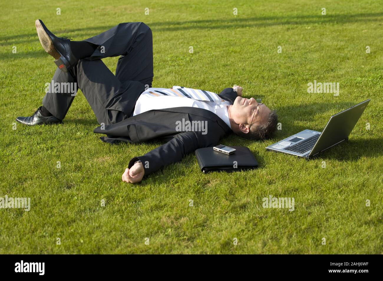 Geschäftsmann sitzt auf einer Wiese, schläft, ruht, Pause, Mittagspause, Burn Out, Laptop, Computer, MR:Yes Stock Photo