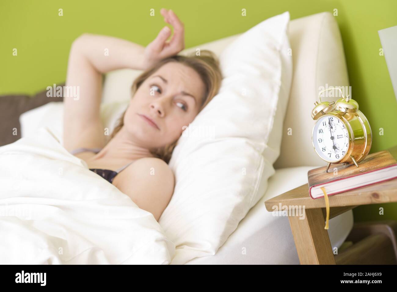 25 -30 jährige Frau schläft im Bett, blickt auf die Uhr, Goldener Wecker, MR:Yes Stock Photo