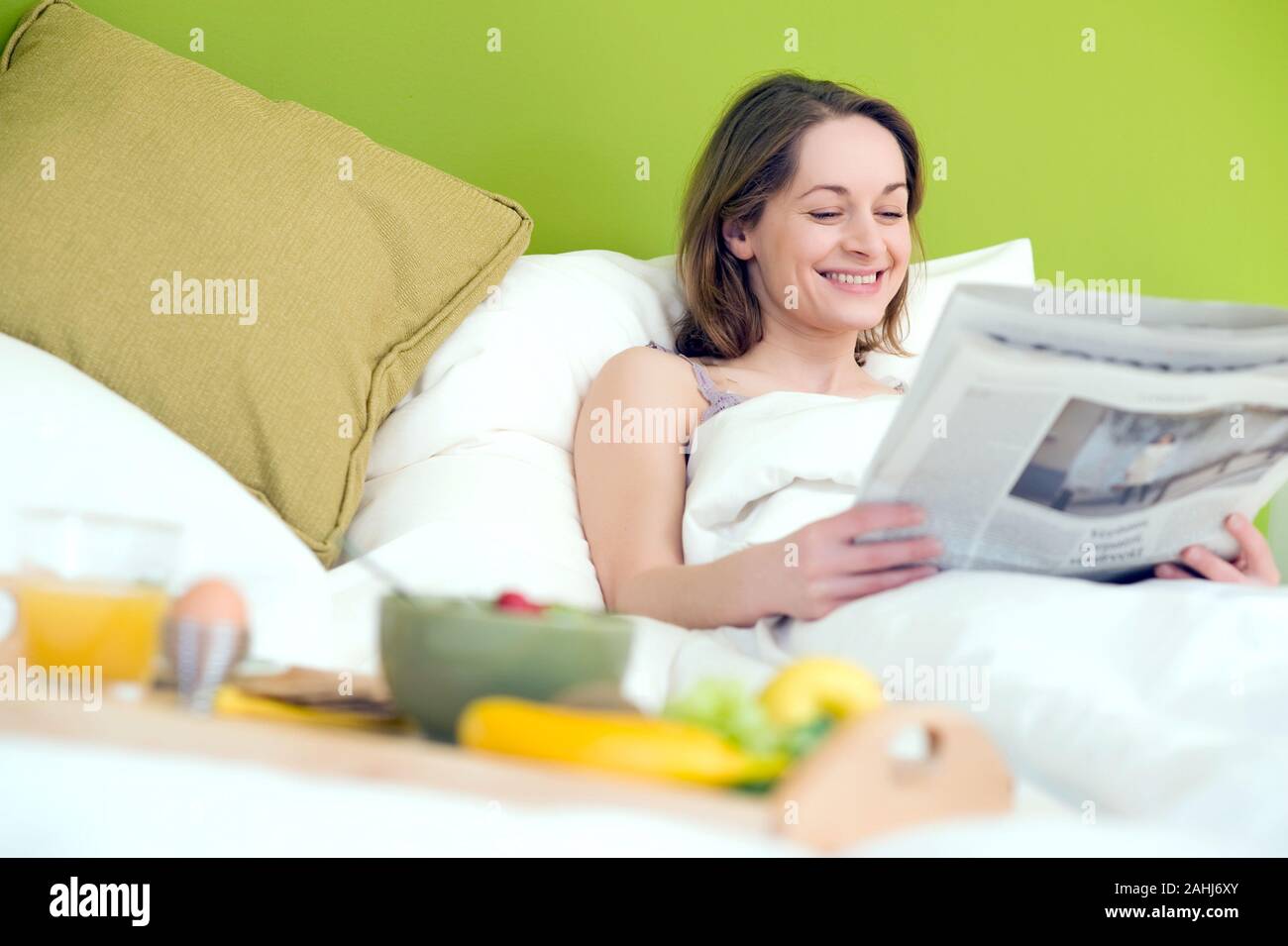 25 -30 jährige Frau schläft im Bett und liest die Zeitung,  MR:Yes Stock Photo