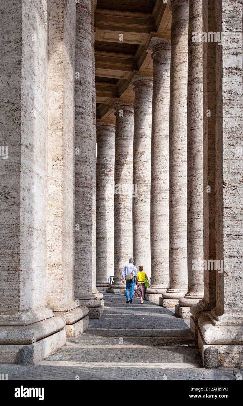 Older middle aged tourist couple walking among tall columns of  Bernini's colonnade in St. Peter's Square, Vatican City, Rome, Italy Stock Photo