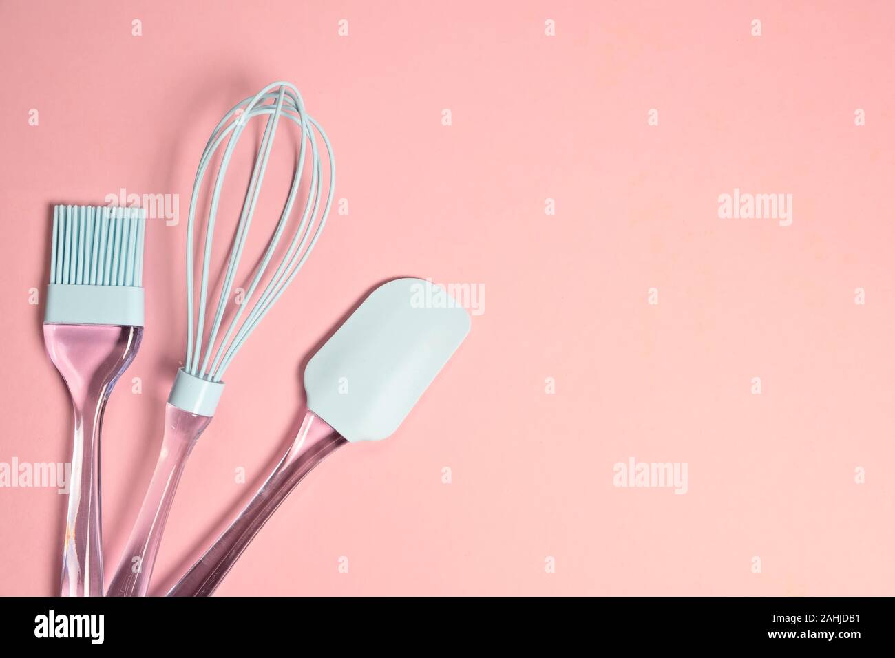 Blue silicone whisk, spatula and brush on light pink background with
