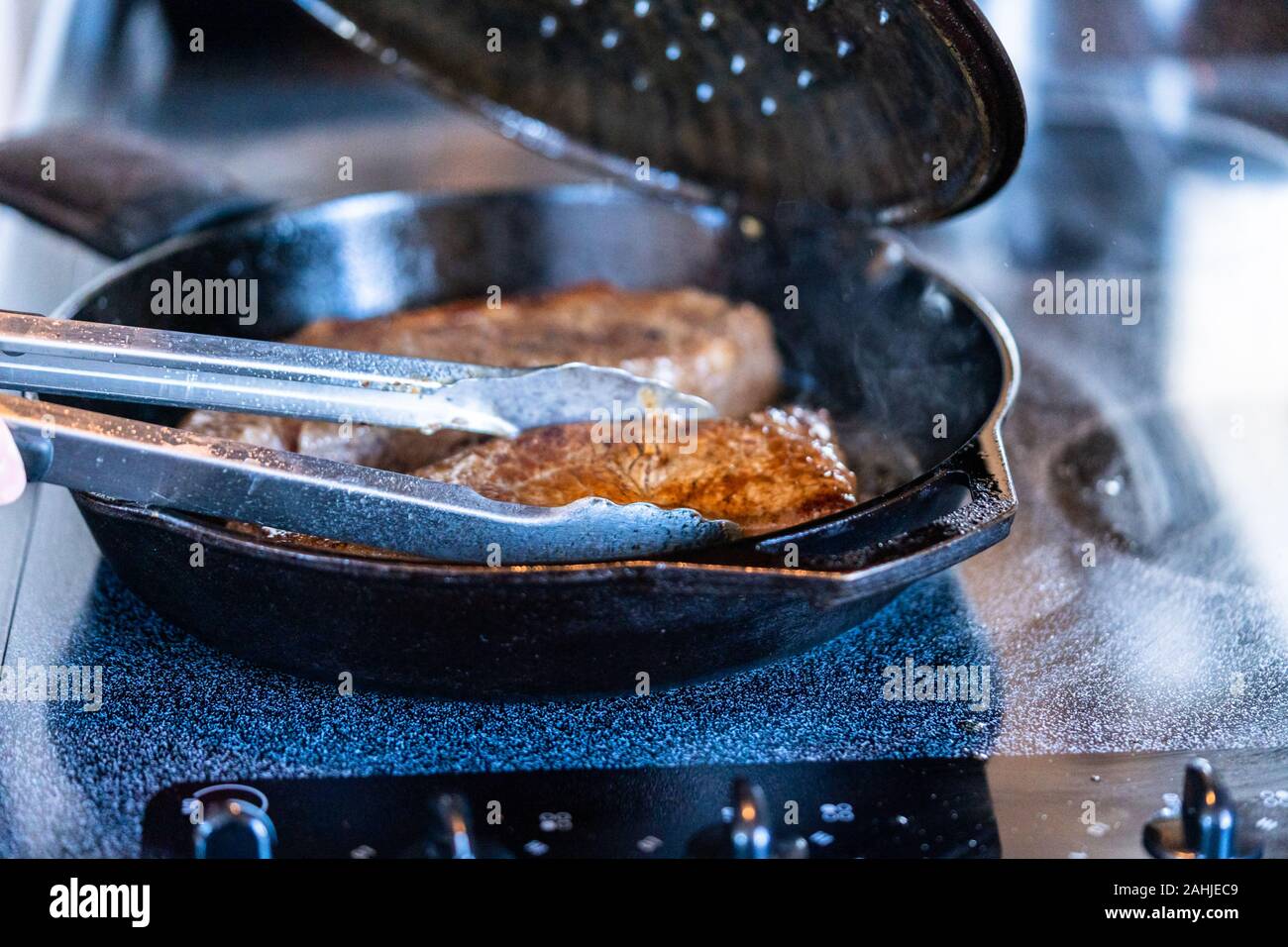 Frying New York strip steak in cast iron frying pan over the electric stove Stock Photo Alamy