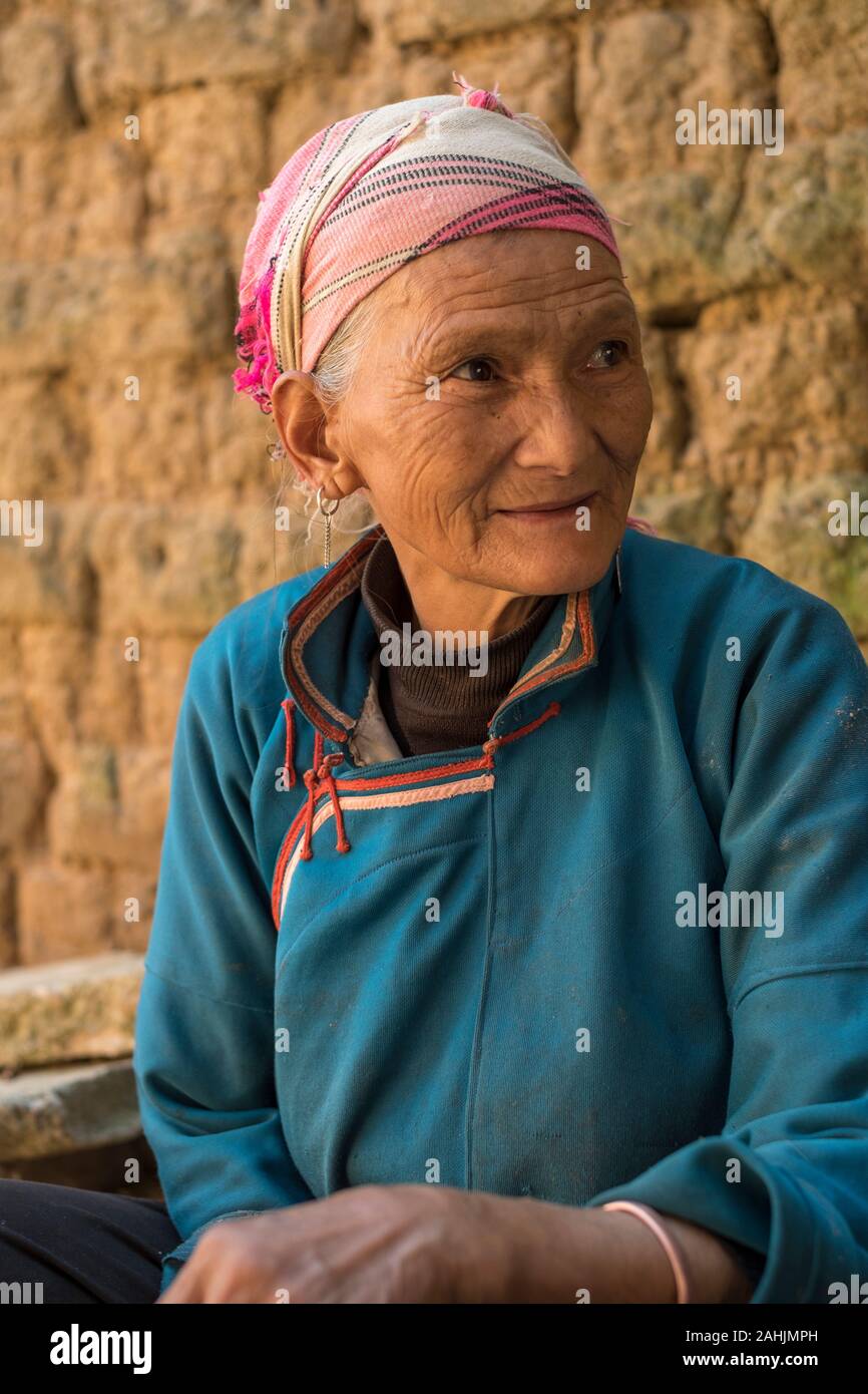 An elderly woman of Yi ethnic group rest in Cangtai village which features traditional earthen dwellings - tuzhangfang, in Honghe, Yunnan, China. Stock Photo