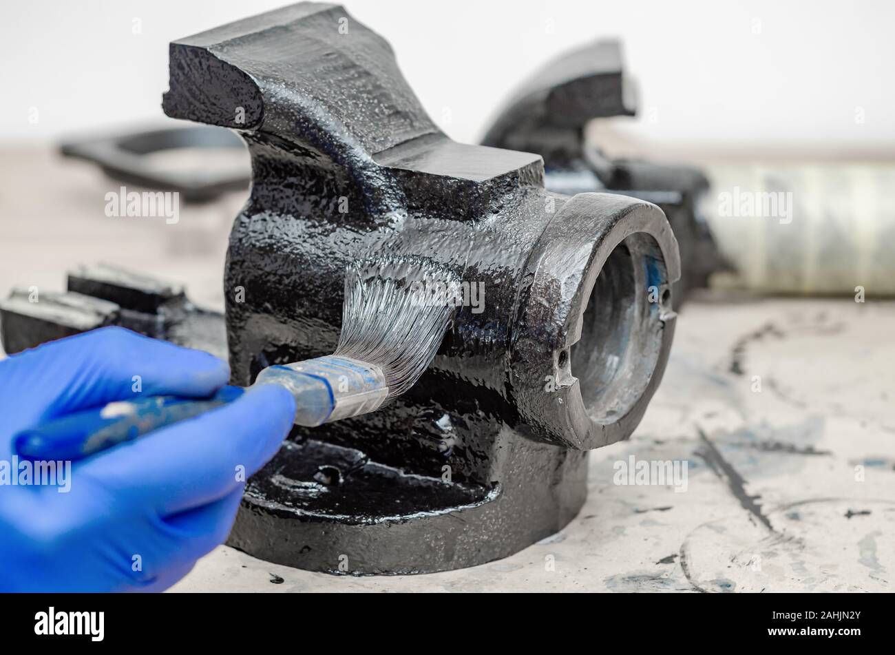 Hand in blue rubber gloves paints metal parts of an old vise with black