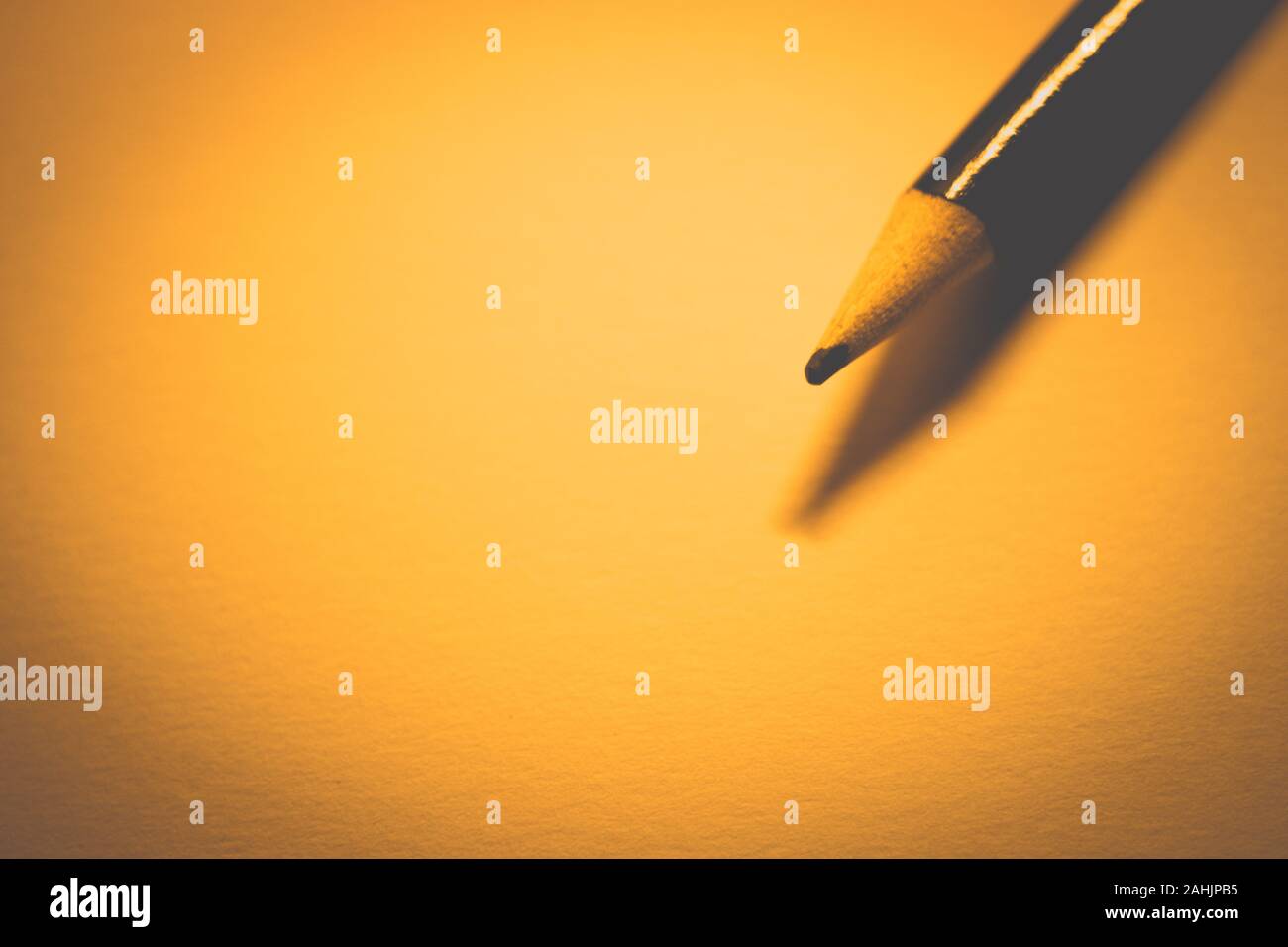 Pencil on clean orange paper, warm tone, copy space. Stock Photo
