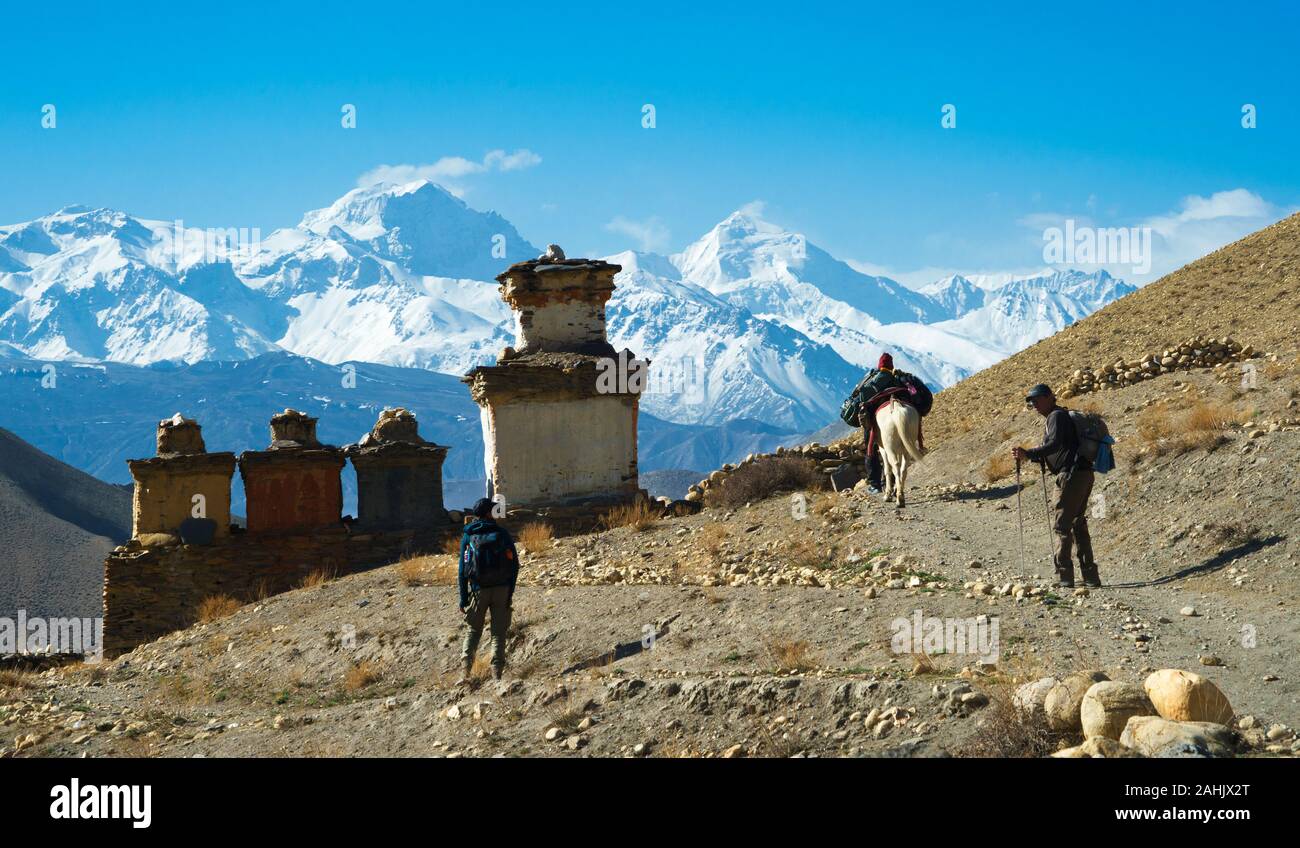 Trekkers and horseman walking towards a buddhist chorten near Dhakmar, Upper Mustang region, Nepal. Stock Photo