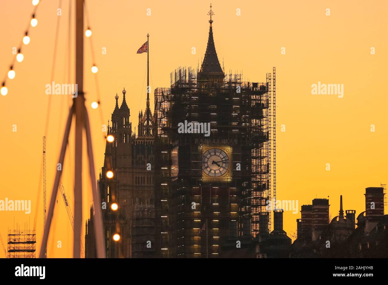 Westminster, London, 30th Dec 2019. The new blue and gold-leaf coloured clock face of the Elizabeth Tower is visible on the Houses of Parliament,  silhouetted at sunset. A beautifully sunny winter day in London concludes with a soft pastel sunset in Westminster. Credit: Imageplotter/Alamy Live News Stock Photo