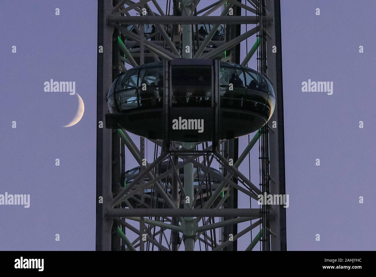 Westminster, London, 30th Dec 2019.The moon is visible behind the London Eye cabins. A beautifully sunny winter day in London concludes with a soft pastel sunset in Westminster. Credit: Imageplotter/Alamy Live News Stock Photo