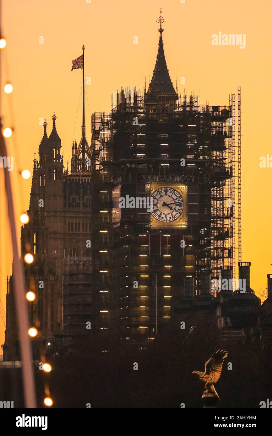 Westminster, London, 30th Dec 2019. The new blue and gold-leaf coloured clock face of the Elizabeth Tower is visible on the Houses of Parliament,  silhouetted at sunset. A beautifully sunny winter day in London concludes with a soft pastel sunset in Westminster. Credit: Imageplotter/Alamy Live News Stock Photo