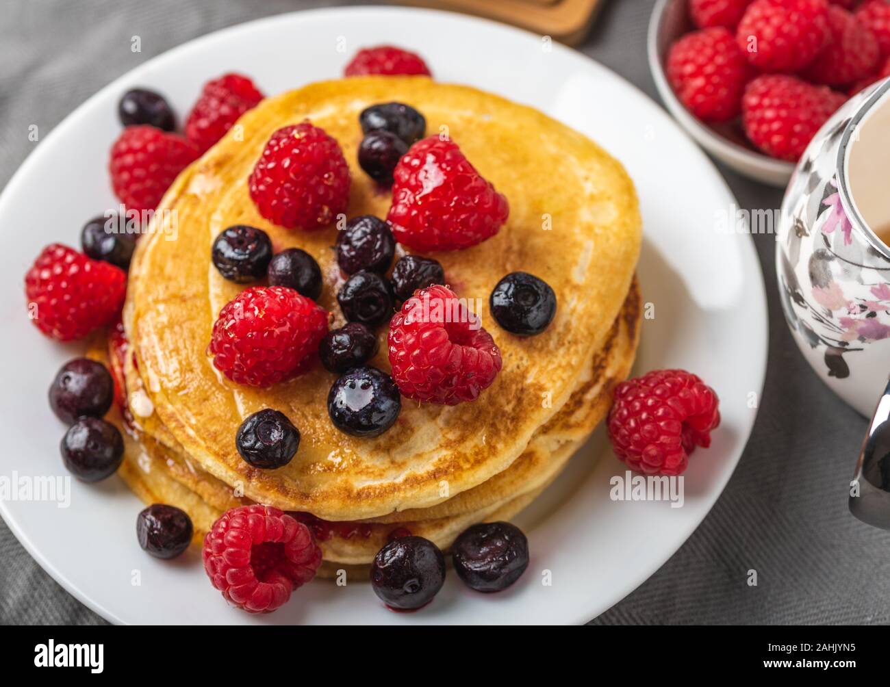 Sweet homemade pancakes with raspberries on white plate on grey table. Stock Photo