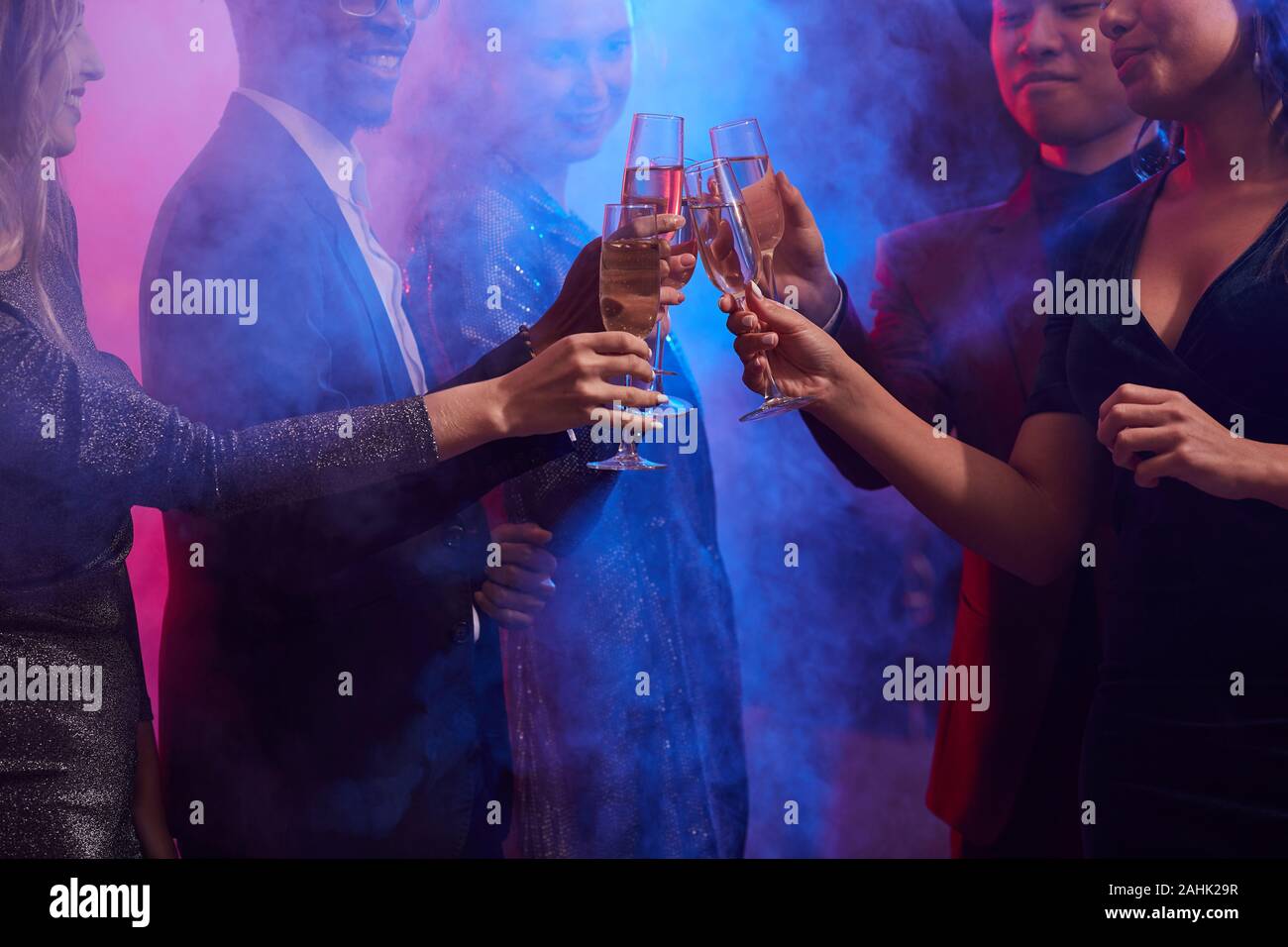 Cropped image of young people clinking champagne glasses in smoky night club while celebrating holidays at party, copy space Stock Photo