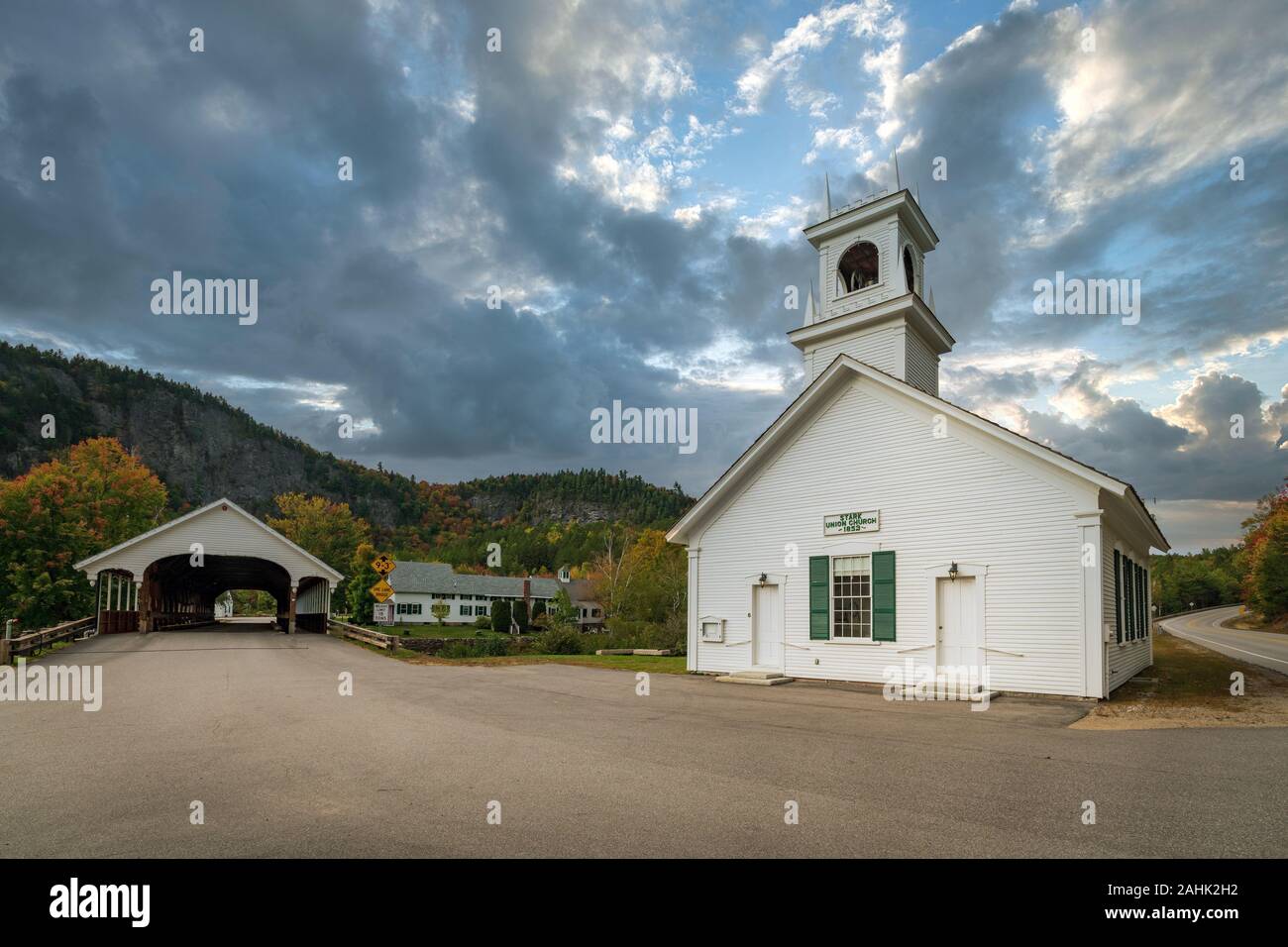 A small white wooden church building and covered bridge make for a quintessential image of a New England Village. Stock Photo