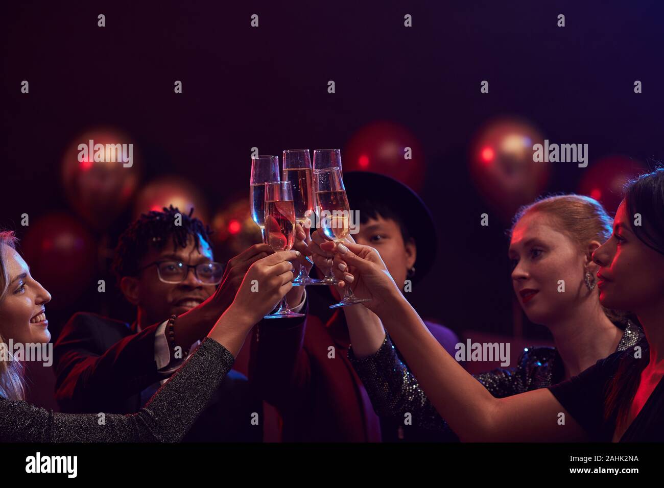 Group of elegant young people raising champagne glasses while enjoying party in nightclub, copy space Stock Photo