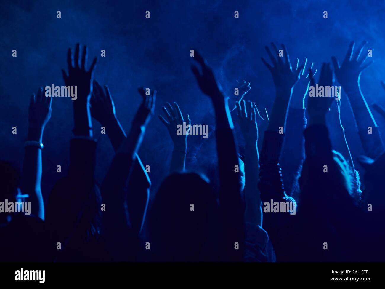 Silhouette of large group of people raising hands while enjoying music concert in smoky nightclub lit by blue light, copy space Stock Photo