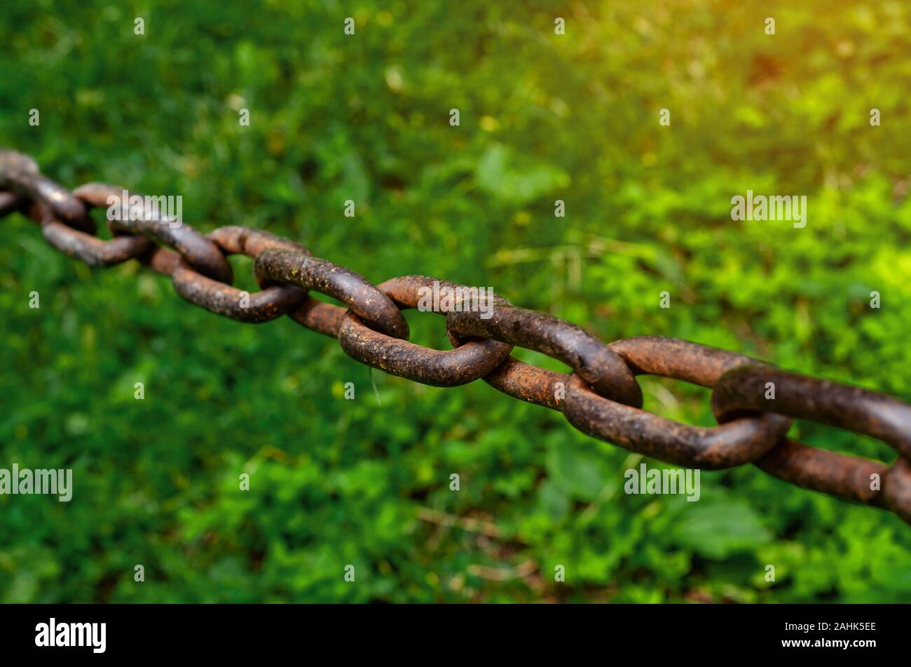 Old rusty chain hanging over green grass background. Stock Photo