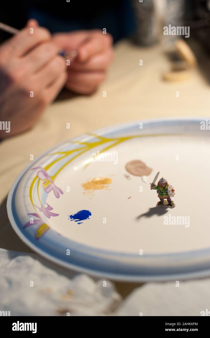 Close-up of hands painting a Dungeons and Dragons (D&D) miniature figure. A mini female Dwarf figure is displayed on a paper plate. Stock Photo