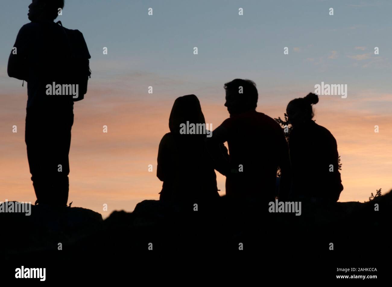 Four people silhouetted and watching a sunset Stock Photo