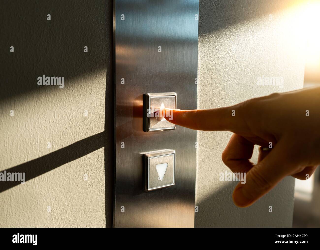 a woman's finger presses the Elevator button in the sunlight Stock Photo