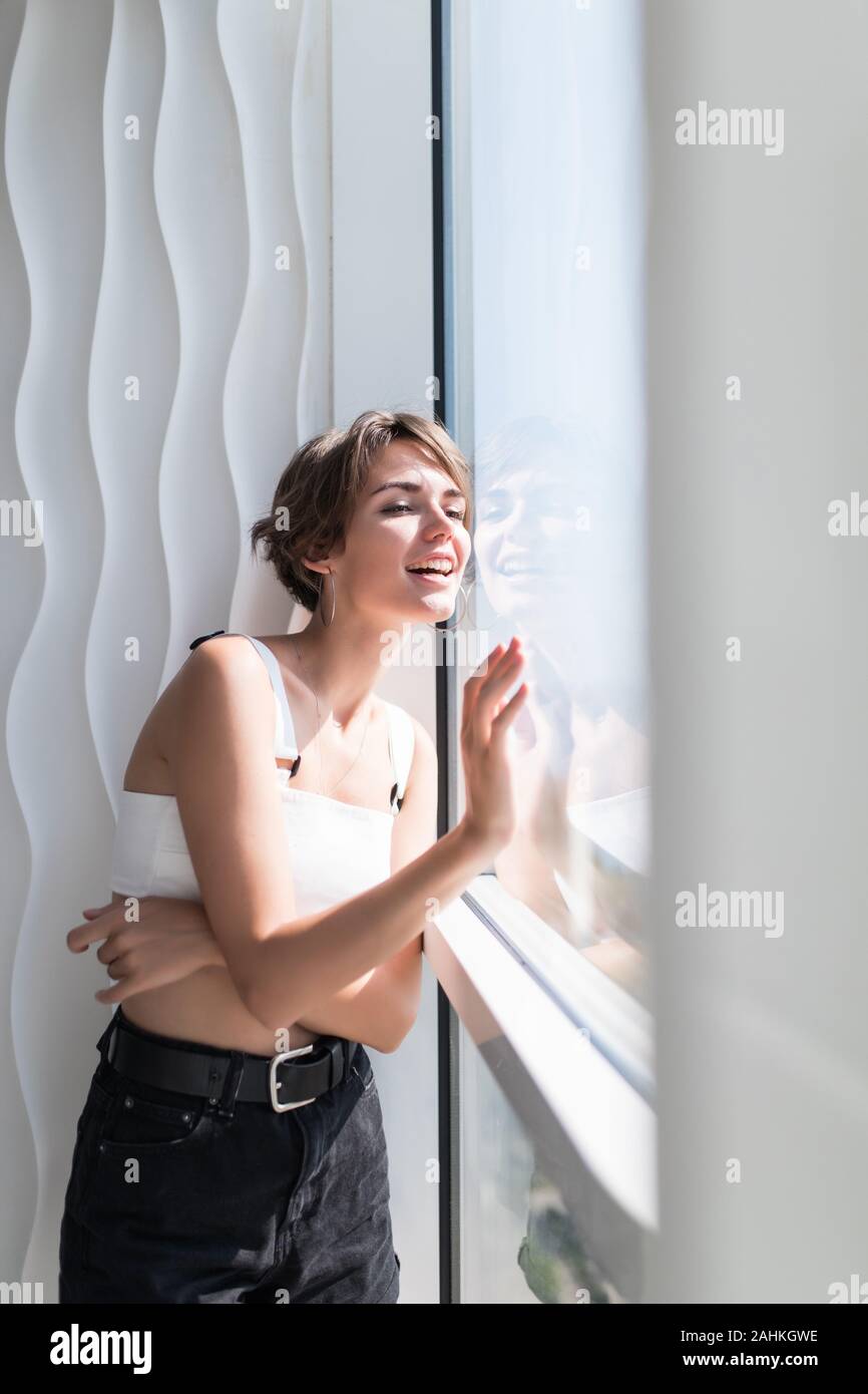 Happy woman thinking and looking at side beside a window at home Stock Photo