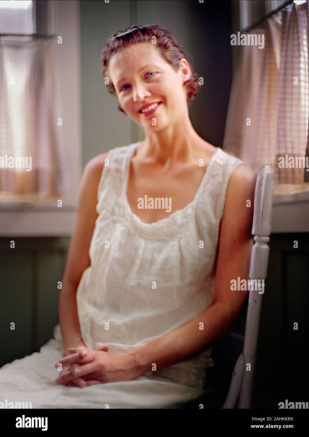 A woman is sitting on a chair inside her house and smiling. Stock Photo