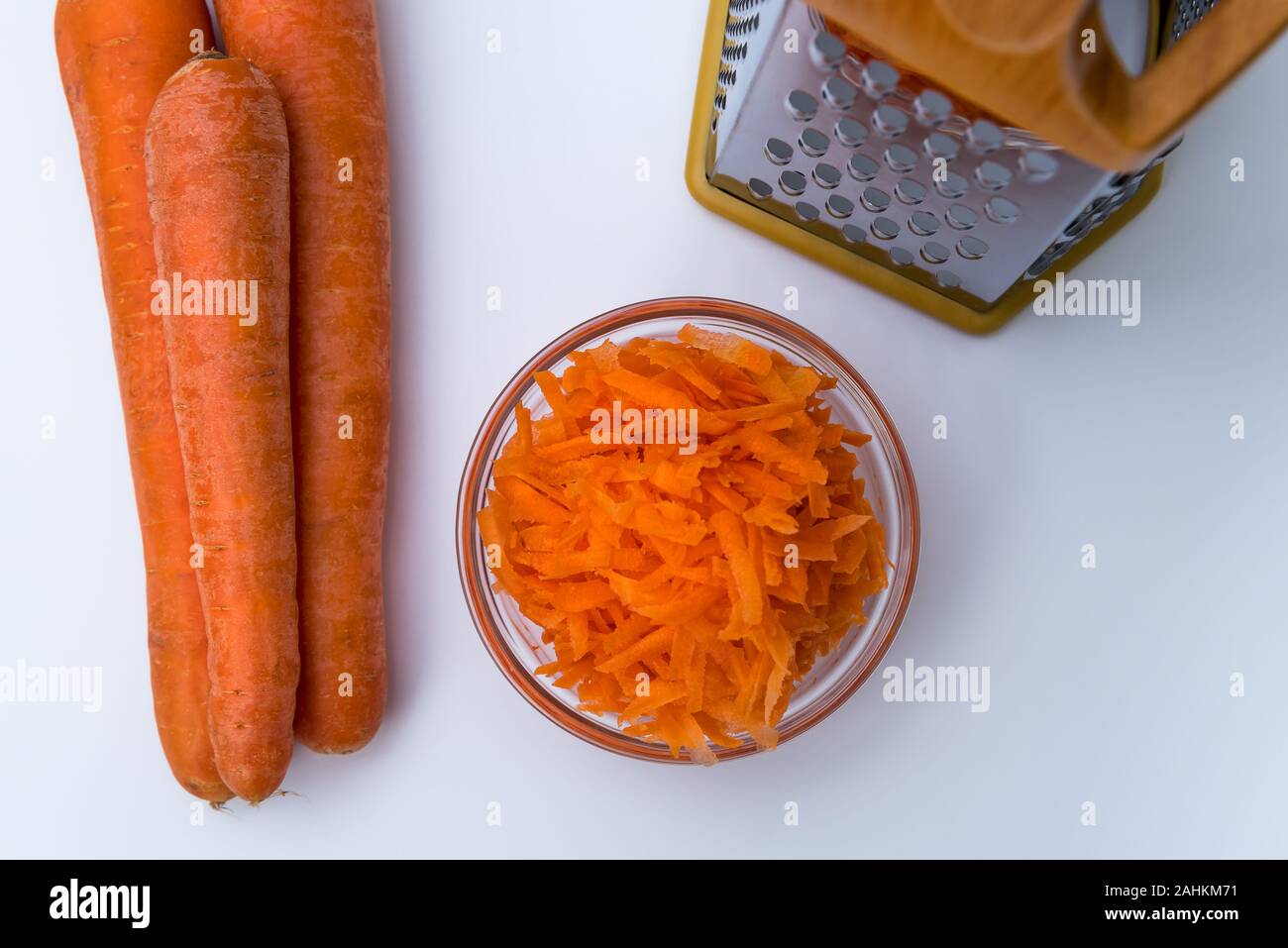 Fresh Grated carrot in a bowl and layout of carrots and grater isolated