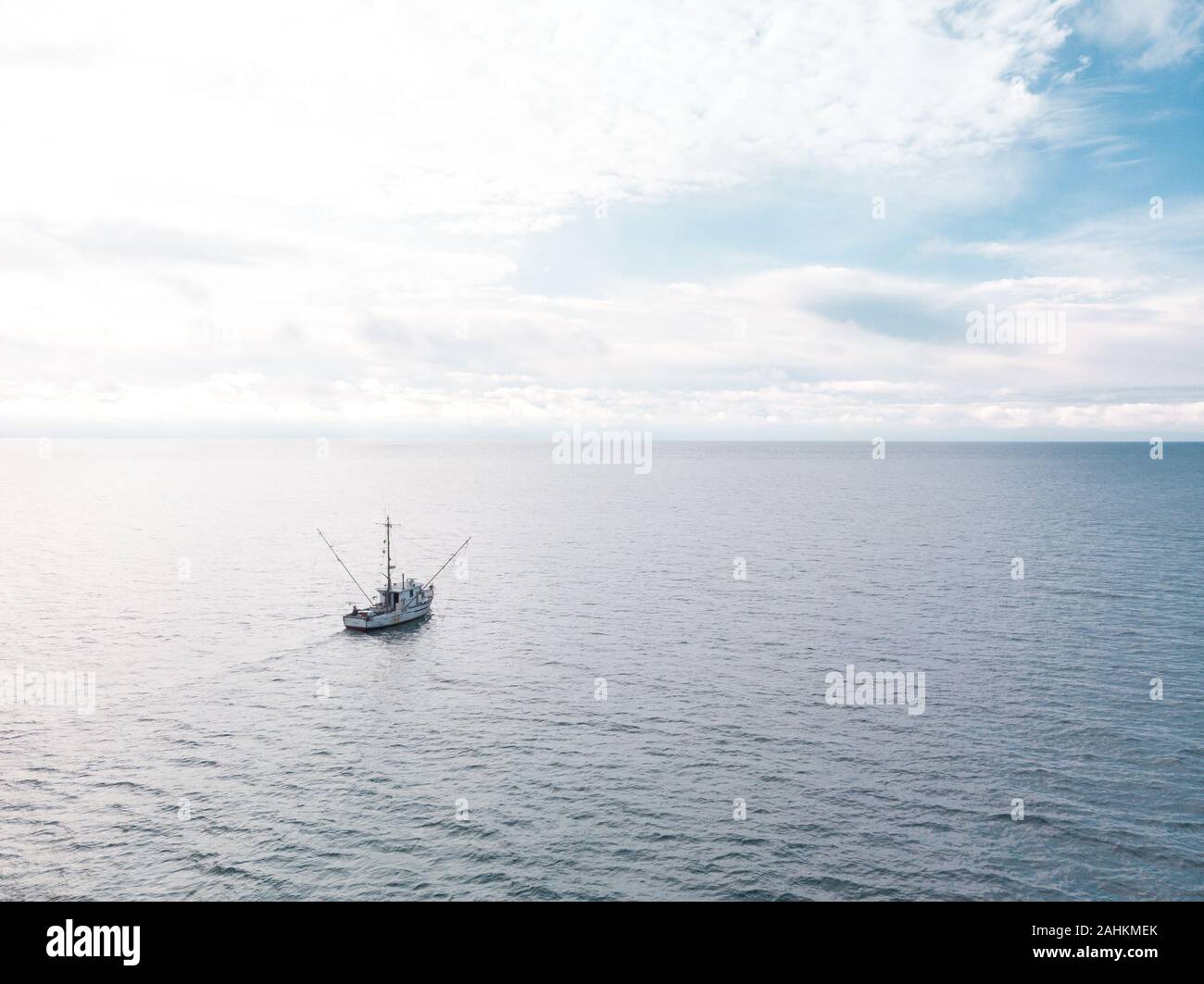 A small old fishing trawler on the open ocean with clouds on the horizon. Stock Photo