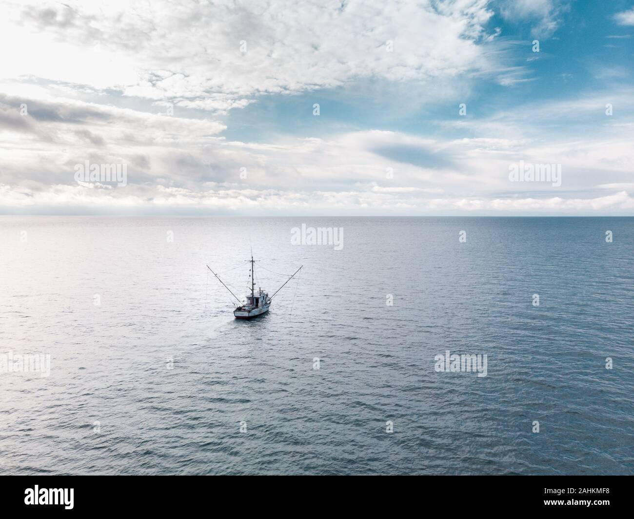 A small old fishing trawler on the open ocean with clouds on the horizon. Stock Photo