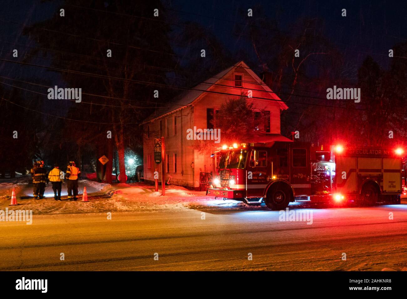 A fire truck and firemen responding to snow storm damage to electrical wires in Speculator, NY USA on a cold winter night. Stock Photo