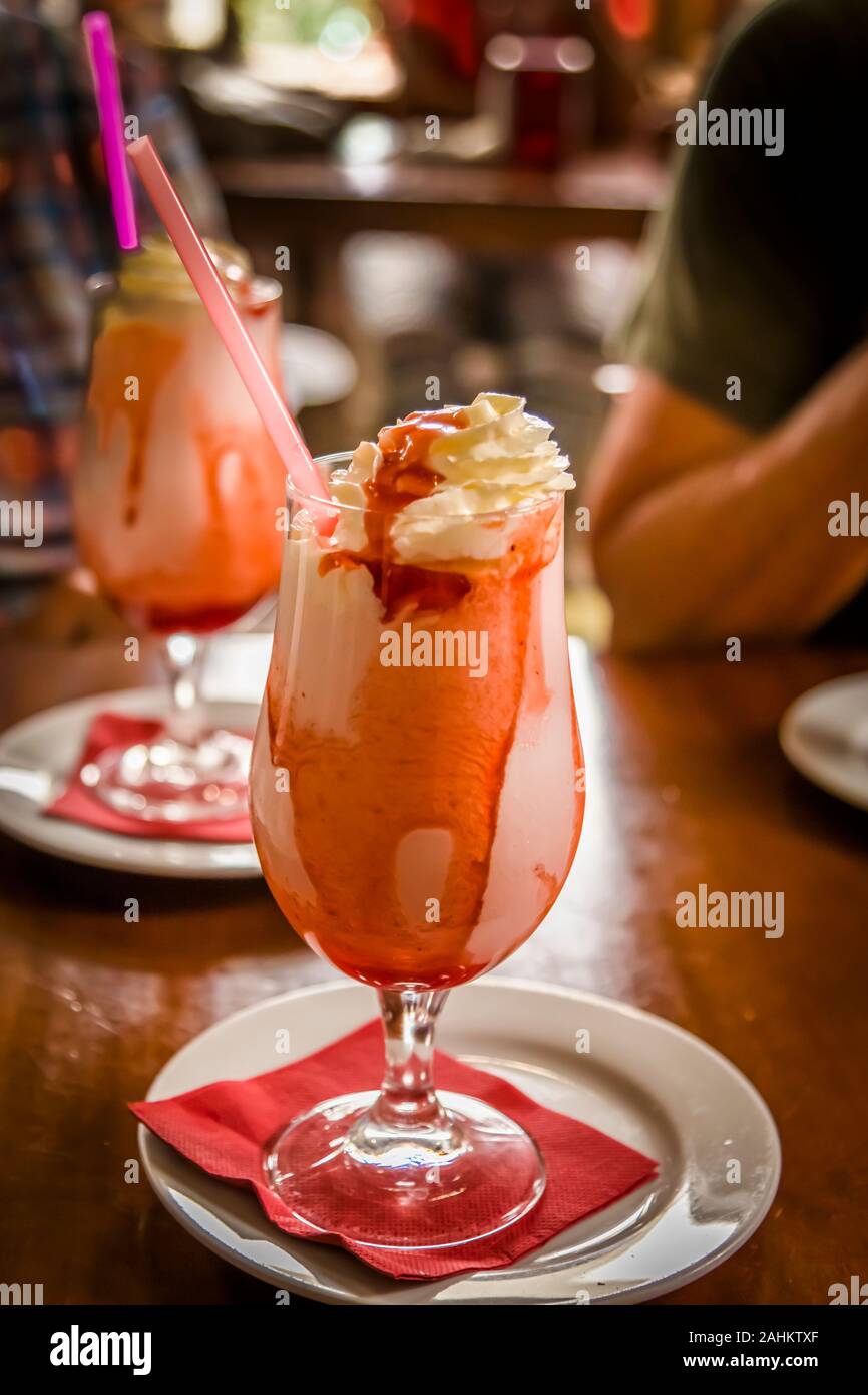 Fancy glass of ice cream with red strawbeery sauce and straw  on table with another galss in background Stock Photo