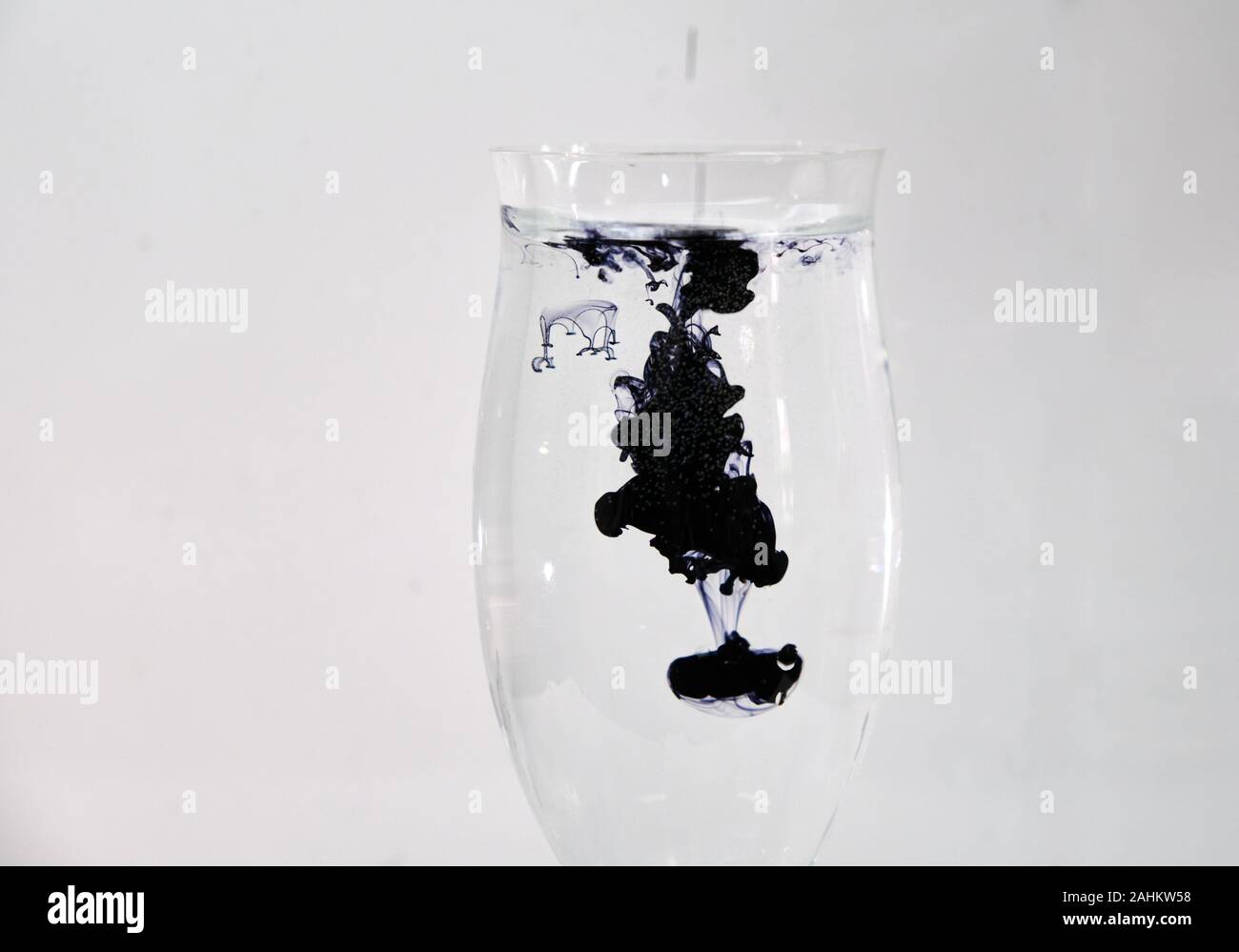 Blue and black ink dropping into a wine glass of water on a white
