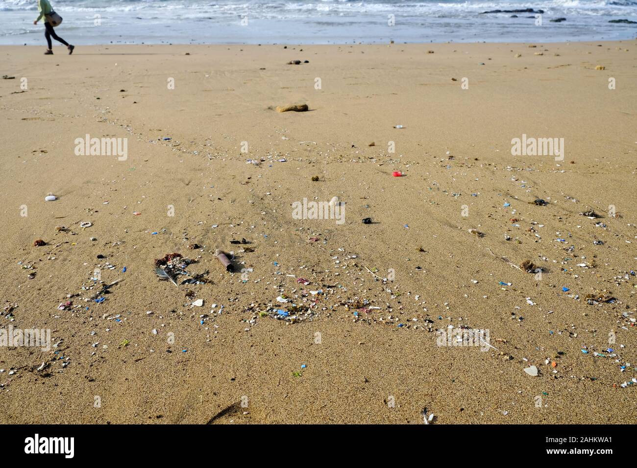 Polluted beach with microplastics and a human figure in the background. Stock Photo