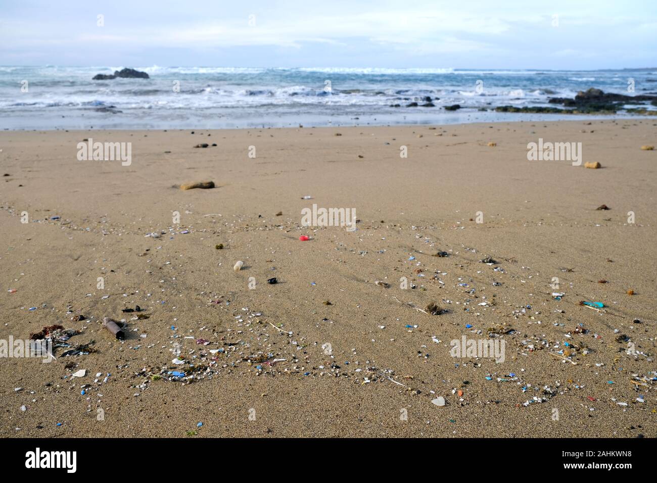 Beach polluted with microplastics, ocean waves in blurred background. Stock Photo