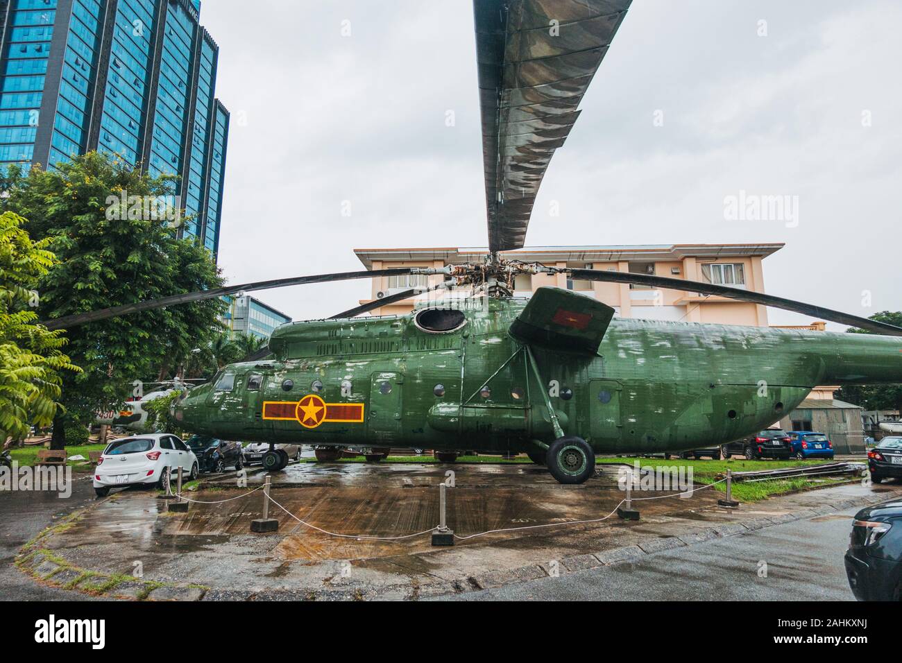 A huge Mil Mi6 Hook-A military transport helicopter dwarfs cars in the rear carpark of the Vietnam People's Air Force Museum, Hanoi, Vietnam Stock Photo