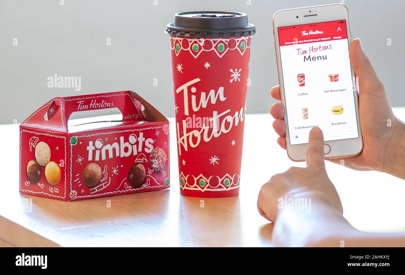 Calgary, Alberta. Canada Dec 28 2019. A person holding an iPhone using the Tim Hortons app with a coffee and a box of Tim Bits during Christmas. Tim H Stock Photo