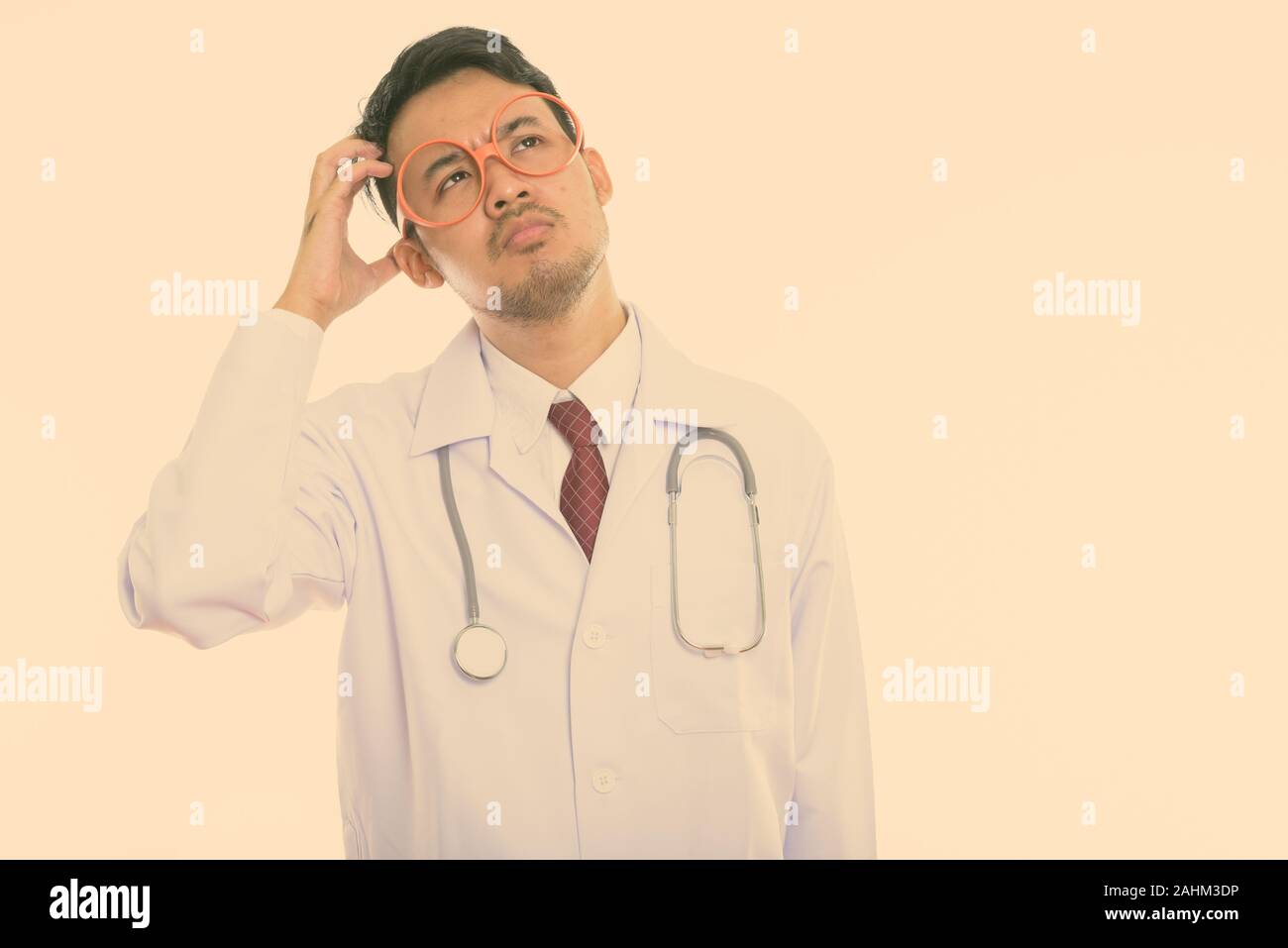 Studio shot of young Asian man doctor thinking while scratching head Stock Photo