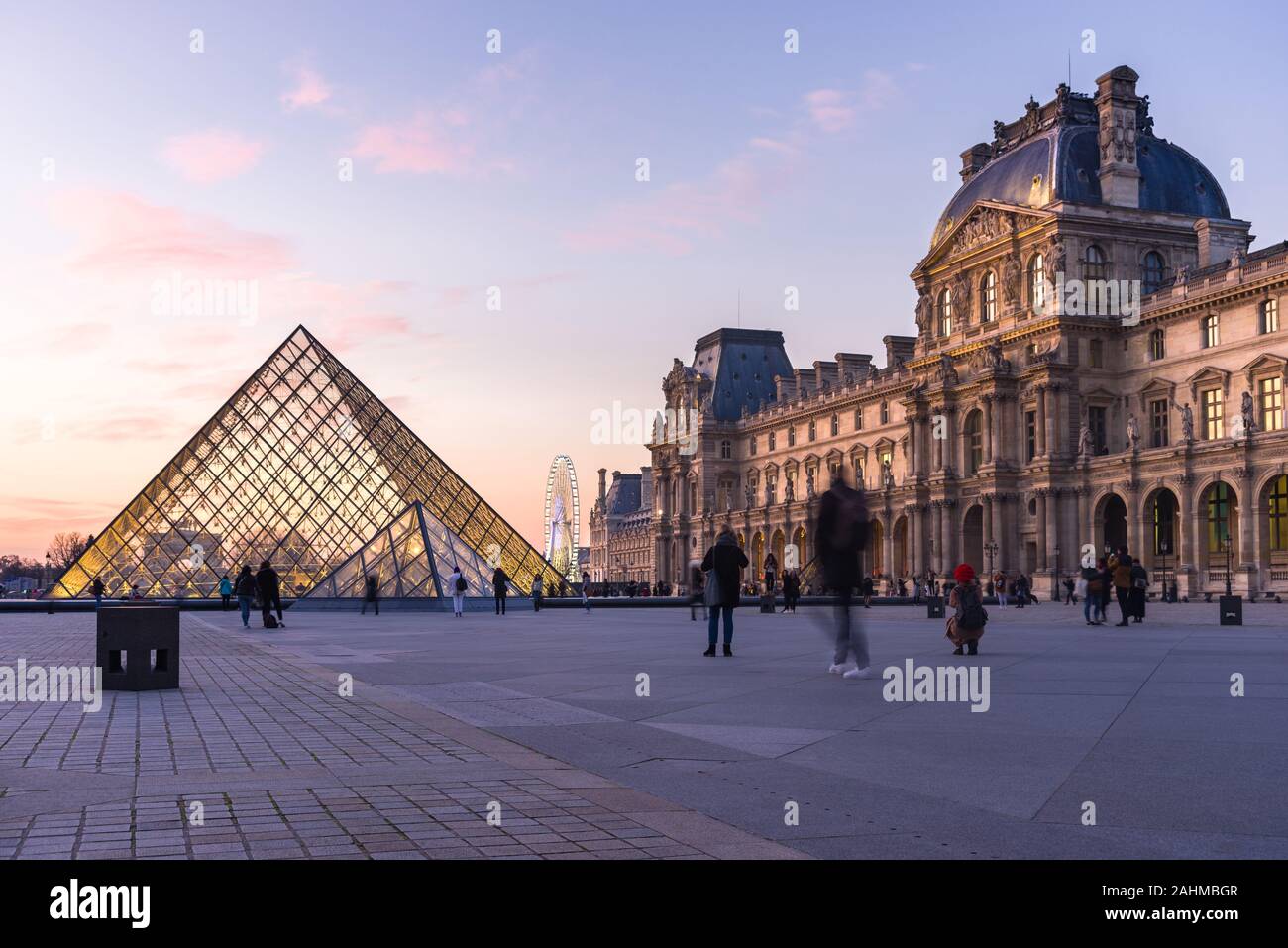 Pyramide du Louvre and Angelina Paris Musée du Louvre at sunset with people walking outside, Paris, France Stock Photo