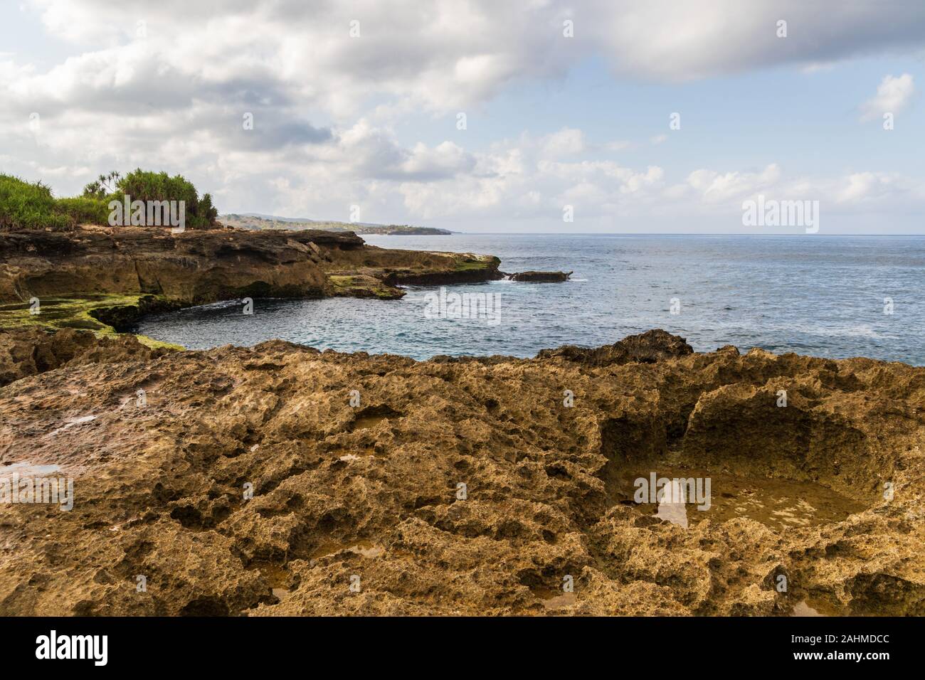 Rocky shoreline at Devil's Tear on island of Nusa Lembongan, Bali, Indonesia. Rocky shore with tidepool in foreground. Shoreline, ocean, sky & clouds Stock Photo
