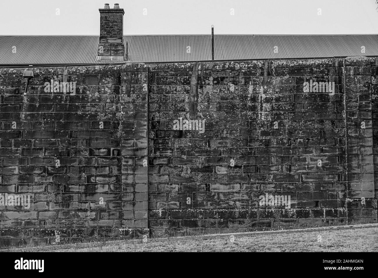 Weathered Sandstone Perimeter Wall of the Former East Maitland Gaol (Jail, Prision, Correctional Centre) with Building and Chimney in Background Stock Photo