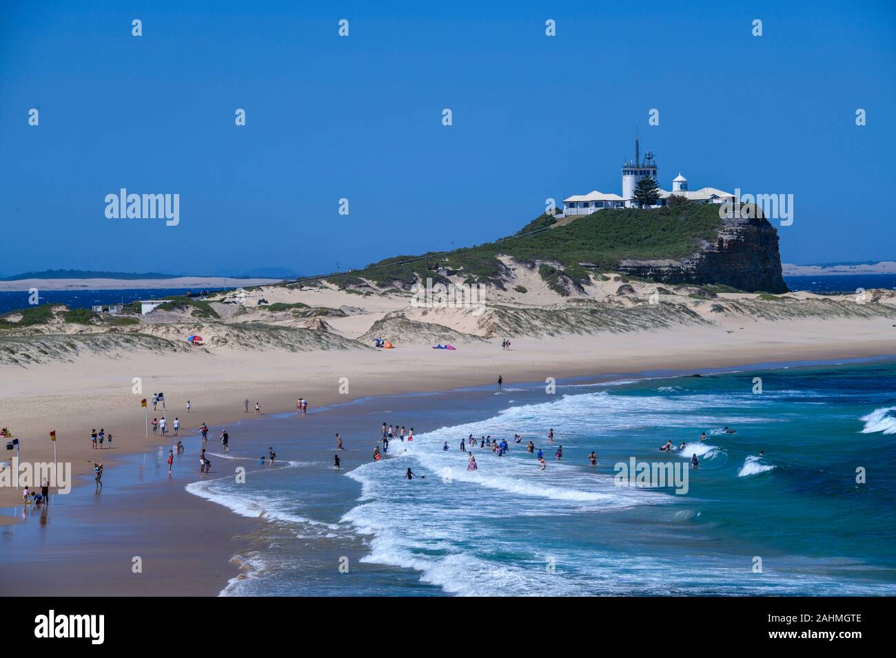 View of Nobbys Head and Beach with People Swimming in Blue Ocean on Sunny Hot Day Stock Photo