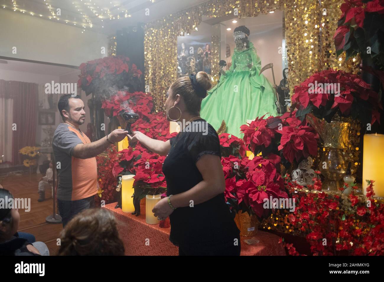 A Santa Muerte priestess hands a smoking cauldron to a man during a home service in Queens, New York City. Stock Photo