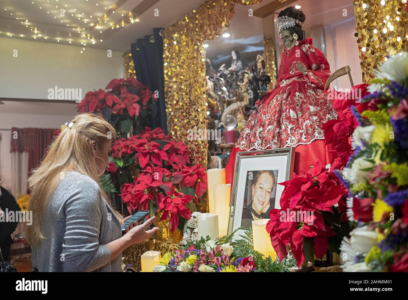A pretty Santa Muerte priestess leads a service in a home temple in Jackson Heights, Queens, New York City. She reads prayers from her phone. Stock Photo