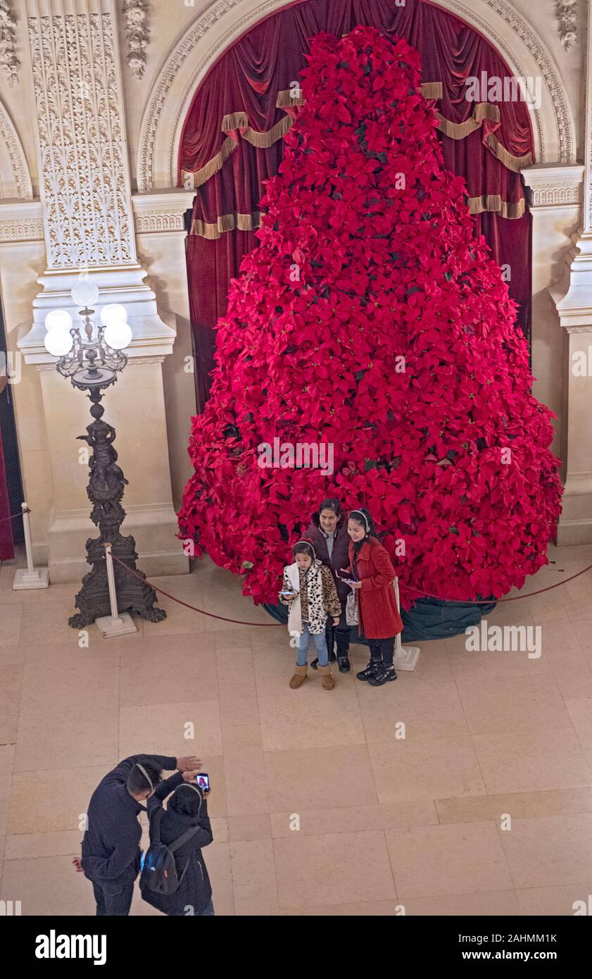 Tourists take cell phone photos in front of an enormous Christmas tree in the Great Hall of the Breakers mansion in Newport, Rhode Island. Stock Photo