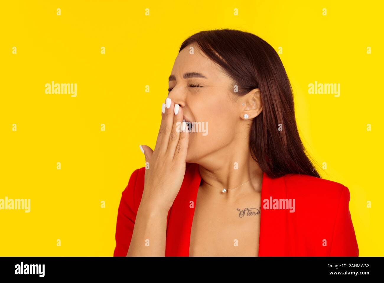 sleepy woman with wide open mouth yawning eyes closed looking bored. Human face expression emotion. Mixed race model isolated on yellow background wit Stock Photo