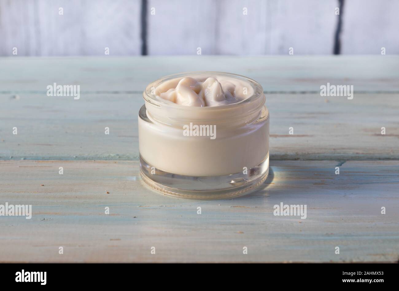 Homemade facial cream of vegetable oils in glass jar, on a light wooden