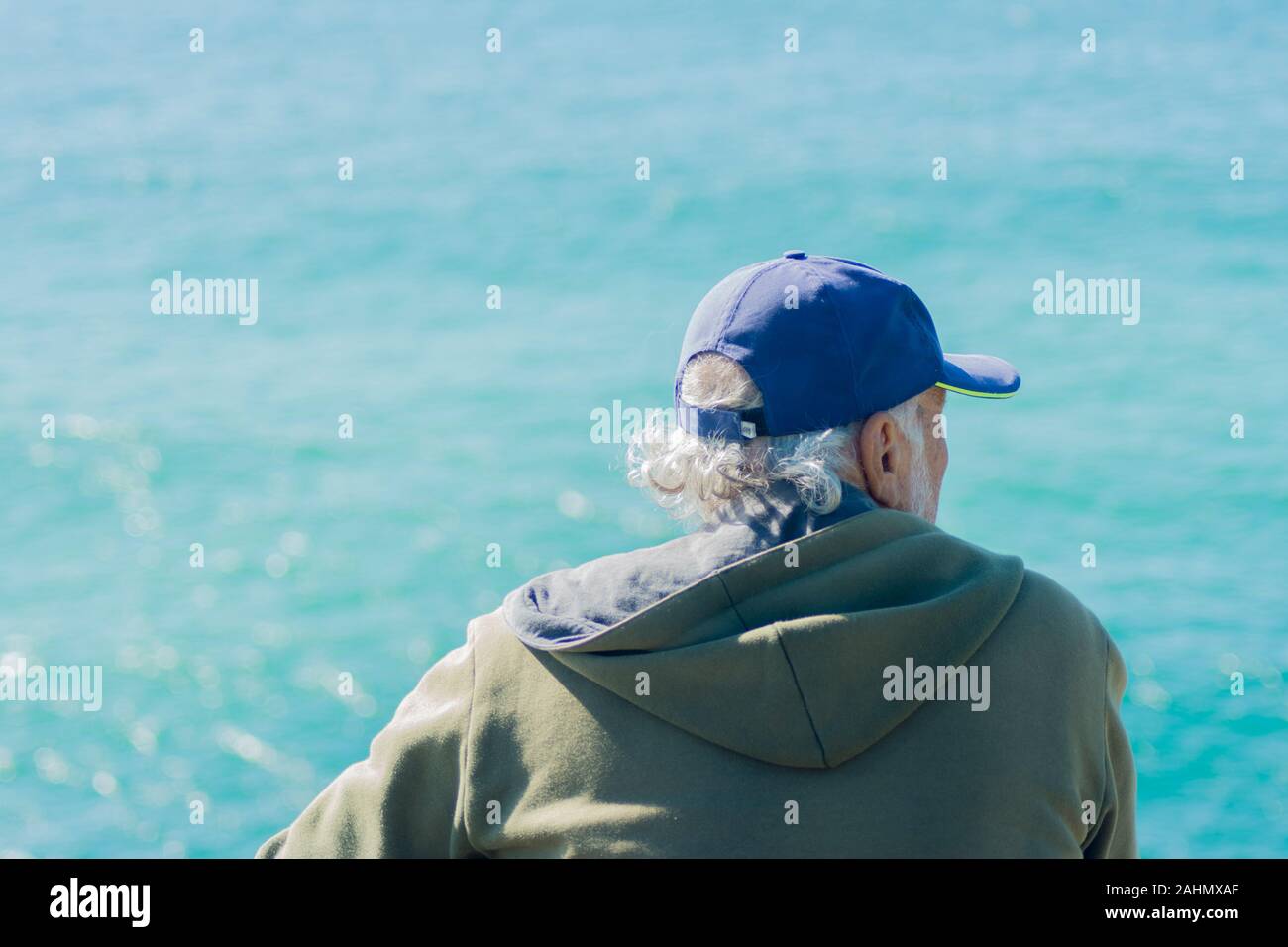 Back view of gentleman wearing sweatshirt and cap looking out at the blue ocean. concept of reflection and good vibes. Stock Photo
