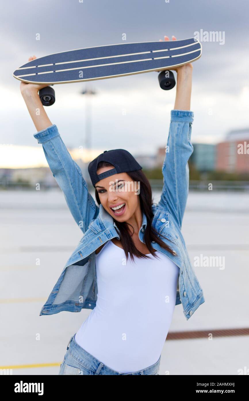 Happy young urban woman holding longboard over head Stock Photo